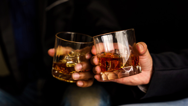 two clinking glasses of whiskey