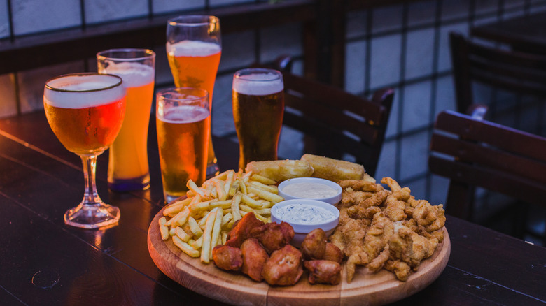 A platter of pub food included French fries and chicken wings, sitting next to several glasses of beer