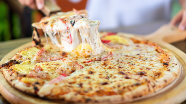 Child lifting piece of pizza from cheesy cooked pie
