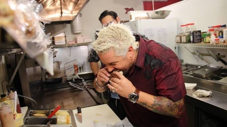 Guy Fieri eating in the kitchen of a restaurant featured on Diners, Drive-Ins, and Dives