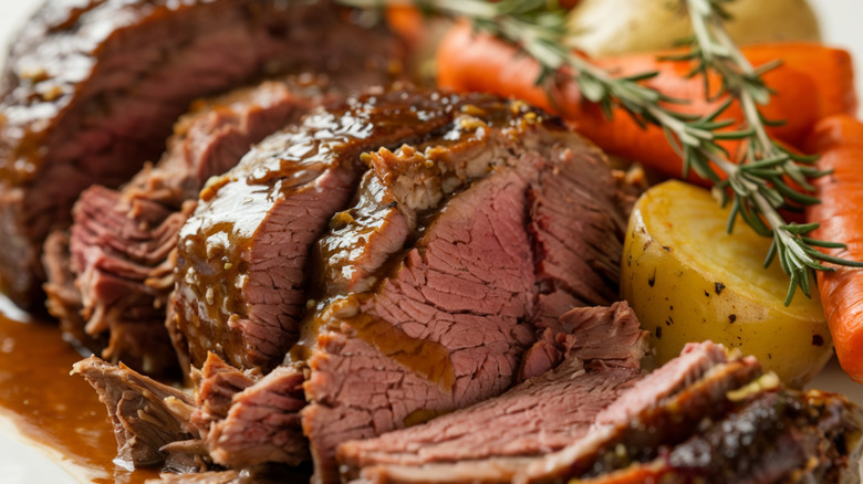 A close-up shot of a pot roast with beef, potatoes, carrots, herbs, and gravy