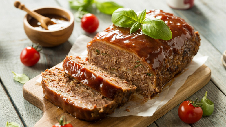 Meatloaf on a cutting board with a tomatoey sauce on top, garnished with basil.