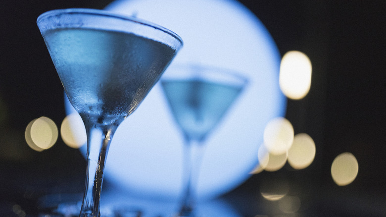 Two martinis resting on a bar, surrounded by ice cubes