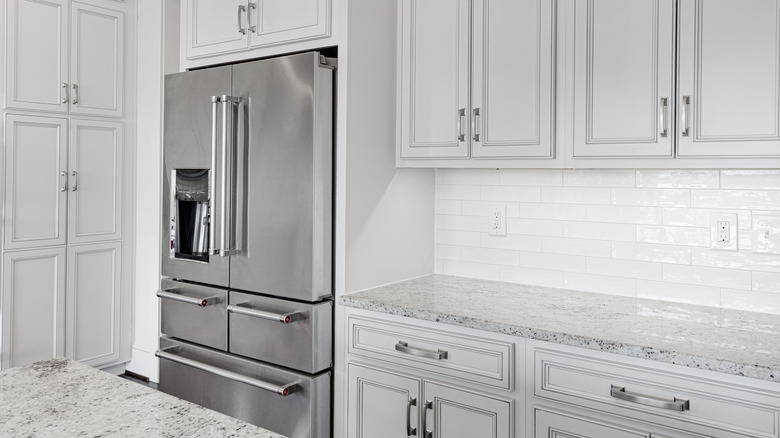 A modern kitchen with white, Shaker-style cabinets, marble counters, and a large stainless steel refrigerator