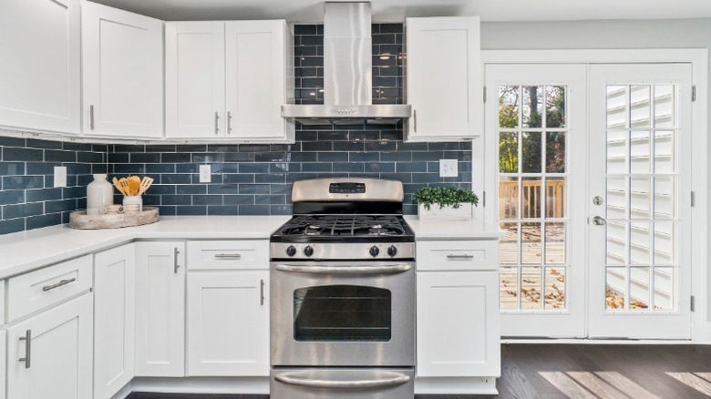 A modern kitchen with white Shaker cabinets, an aqua-colored backsplash, a stainless steel oven, and doors leading to a patio