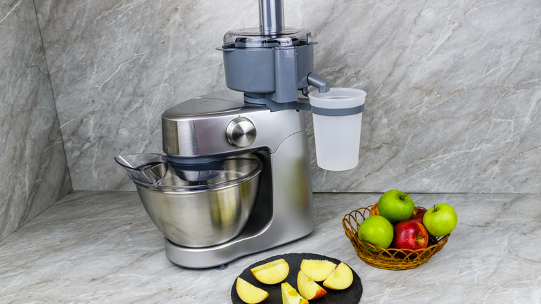 A stainless steel food processor with apples on a counter.