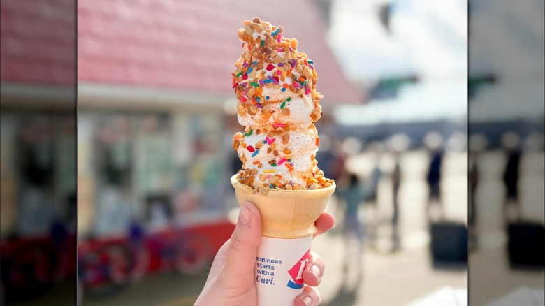 A person is holding an ice cream cone outside of a Dairy Queen.