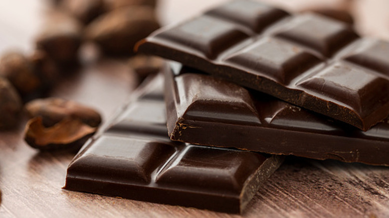 Dark chocolate bars laying in a pile beside cacao nibs