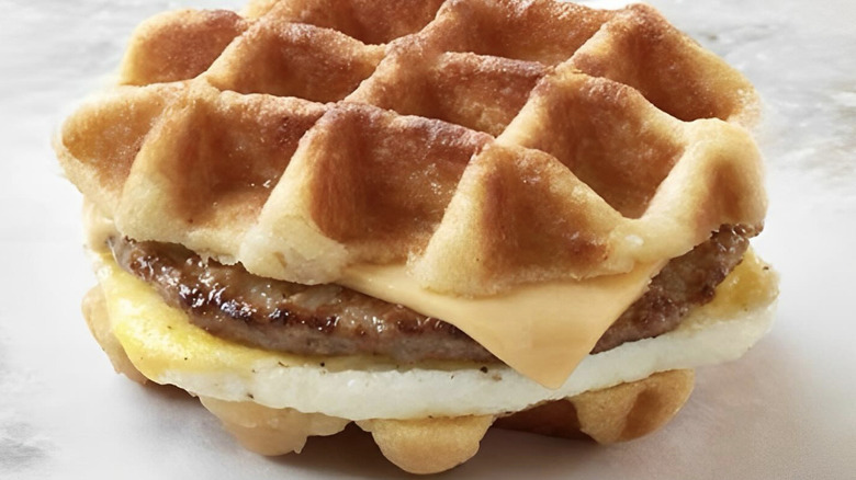 Hand holding Jack in the Box waffle breakfast sandwich
