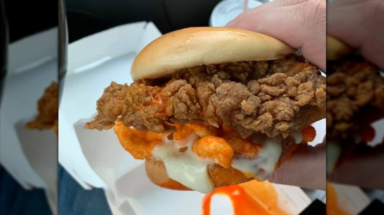 Hand holding Cheetos chicken sandwich with sauce mess in box underneath