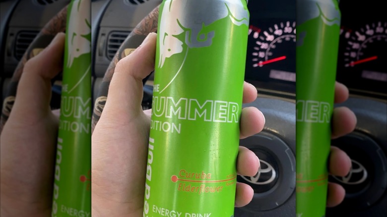Mirrored image of hand holding Curuba-Elderflower Green Edition Red Bull can in front of steering wheel