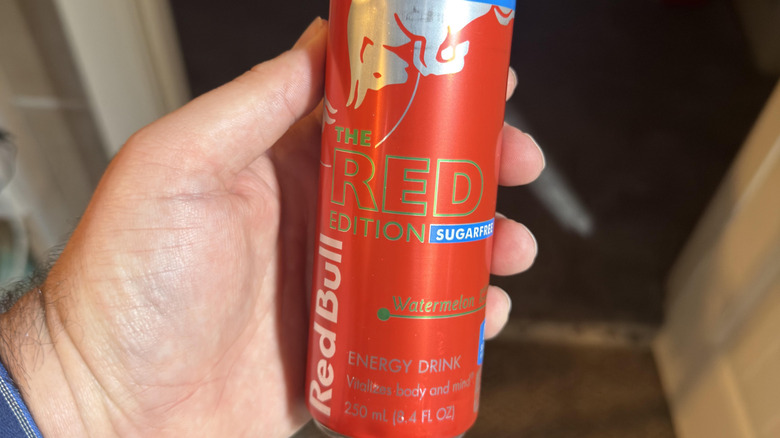 Close up of hand holding Sugarfree Watermelon Red Edition Red Bull can in front of door