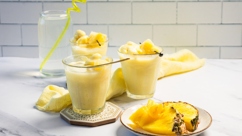 Three glasses of Dole Whip float with pineapple and a glass of coconut water in background.