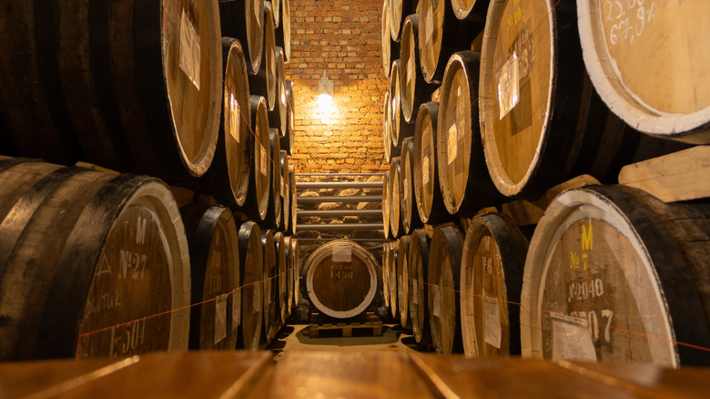 Barrels with stamped information shown stacked in a dimly lit brick warehouse