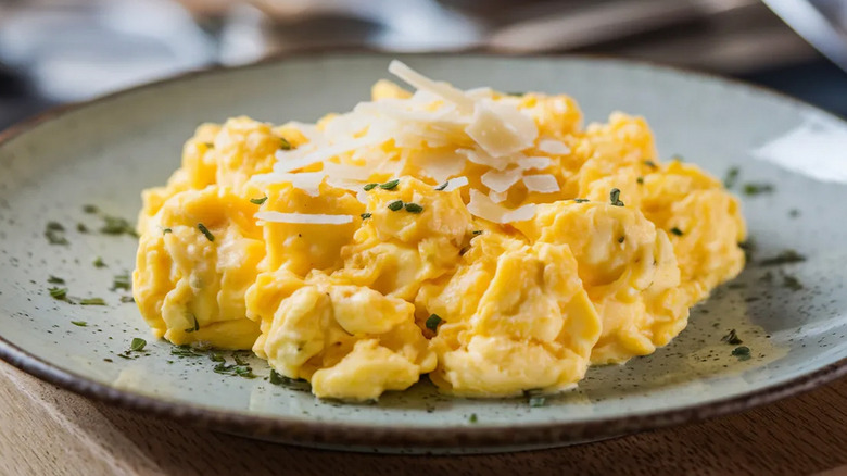 A plate of creamy scrambled eggs topped with shaved cheese and herbs