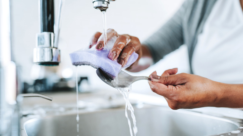 A person washing a spoon with a soapy sponge