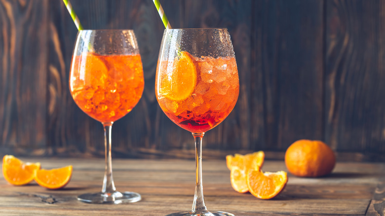 Two Aperol spritzes over ice with straws on a table surrounded by orange slices