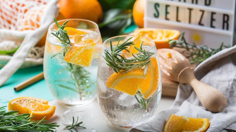 Two glasses of seltzer with orange slices, rosemary sprigs