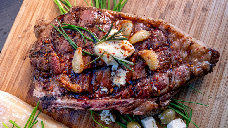 a grilled ribeye topped with butter, garlic, and rosemary on a wooden cutting board