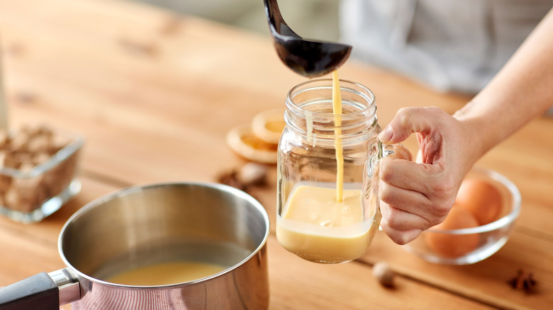 A glass of eggnog being poured, with holiday flourishes
