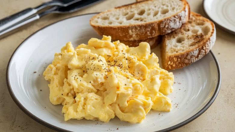 Overhead view of soft, creamy scrambled eggs on a plate with bread