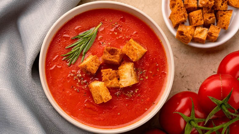 red tomato soup in a bowl with rosemary and croutons