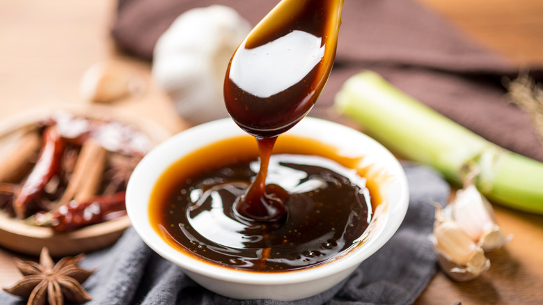 soup spoon drizzles oyster sauce into white bowl