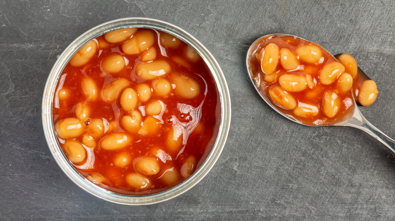 Overhead shot of open can of beans beside spoonful of beans.
