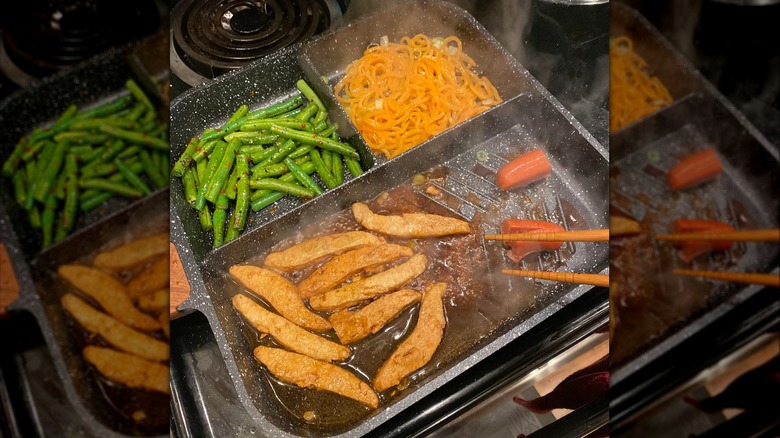 Overhead view of cooking veggies, meat, and noodles on a divided pan