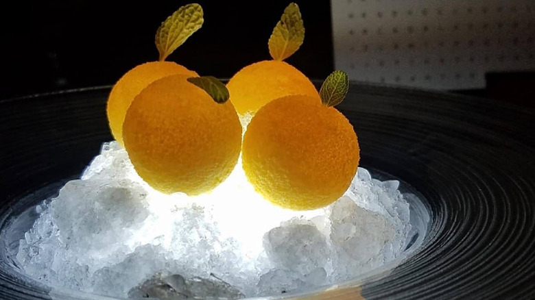 Four orange coco butter shells topped with micro sage on illuminated ice