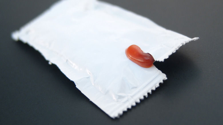 unlabeled packet of ketchup slightly torn open with a bit of ketchup coming out at the rip