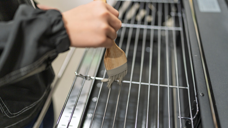 A person brushes oil on a new bbq grill grate.