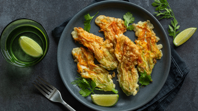 a plate of fried squash blossoms next to some raw on a table