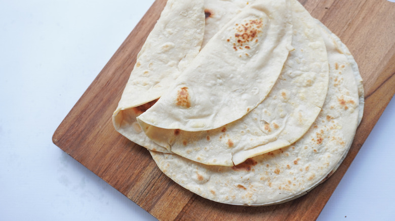 A stack of flour tortillas on a wooden cutting board