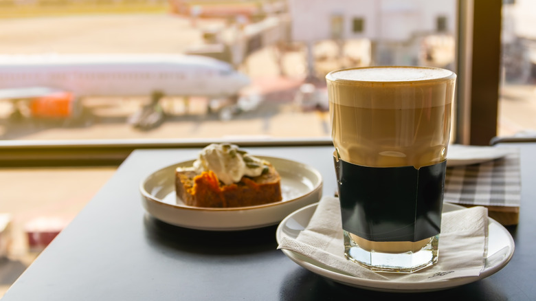 Coffee and breakfast pastry on airport table with plane outside window