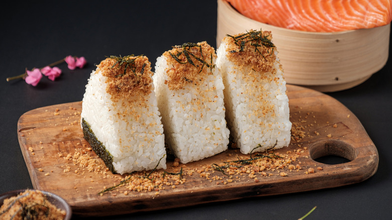 Three rice balls topped with furikake on a wooden serving board