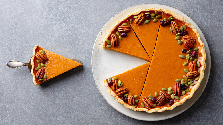 Pumpkin pie with a slice removed rimmed by nuts