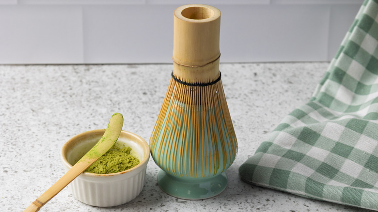 Close-up of a matcha whisk holder with whisk and bowl of matcha on kitchen counter