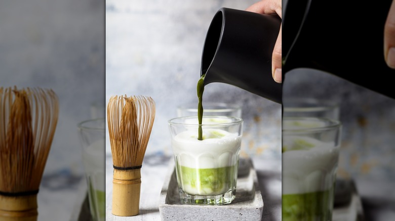 View of person pouring matcha into a glass next to an upright matcha whisk