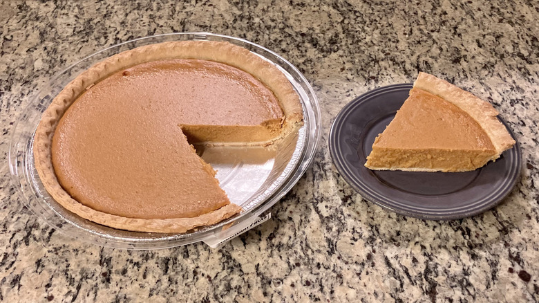 A whole Sam's Club's Member's Mark Pumpkin Pie sits next to a slice of the pie on a purple plate