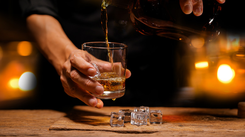 Bartender pouring bourbon into a rocks glass with ice