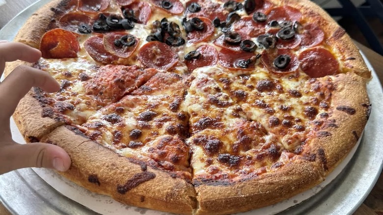 Closeup of person grabbing slice of Greek-style pizza