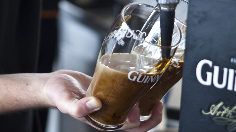 A bartender pours two pints of Guinness at an angle in a pub in Dublin