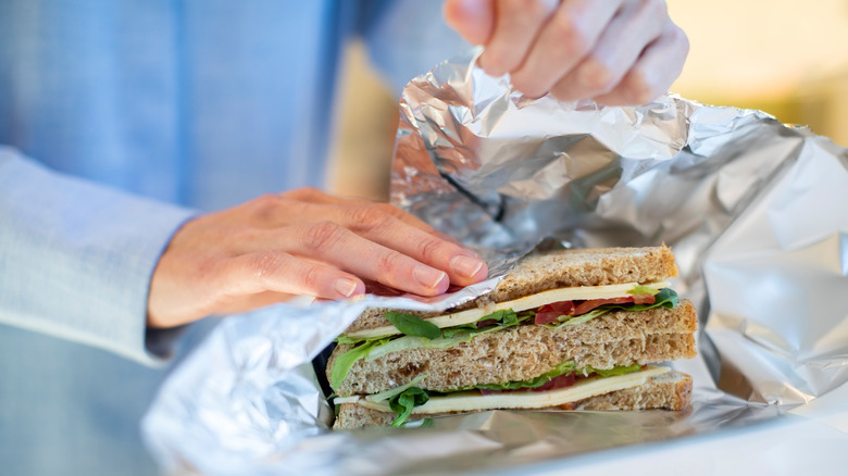 person wrapping a sandwich in aluminum foil