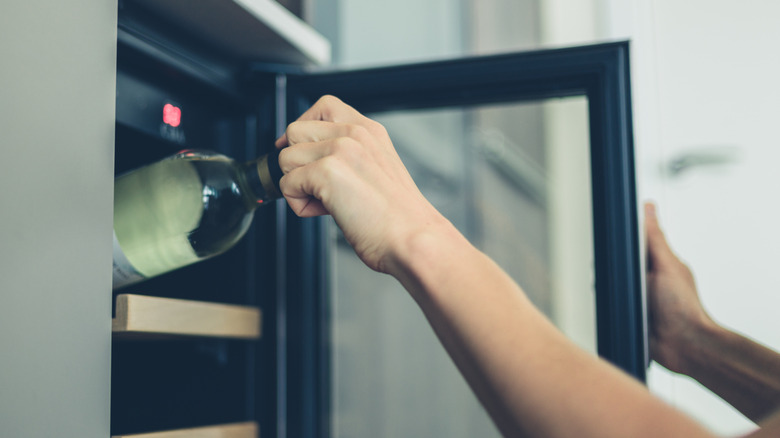 Someone taking a bottle of wine out of a wine fridge