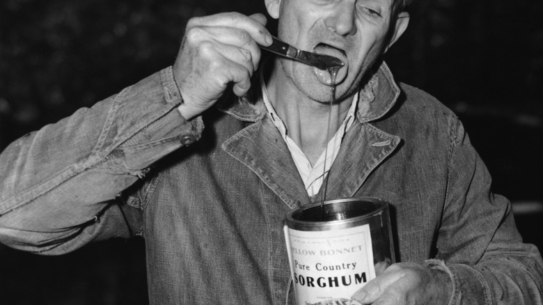 A historical image of a man eating from a can of molasses off a pocket knife