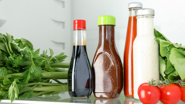 Bottles of condiments and veggies on a fridge shelf