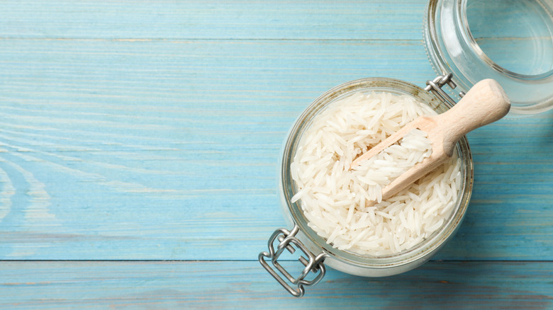 Overhead view of open jar of white rice with wooden scoop