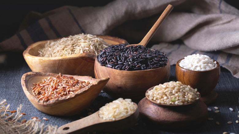 Different varieties of uncooked rice in wooden bowls
