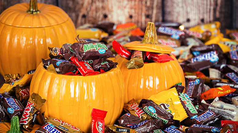 Ceramic orange pumpkin-shaped containers overflowing with small candy bars set out for Halloween